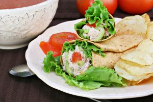 Healthy tuna salad wraps with a side of chips.  Bowl of tomato soup and fresh tomatoes in the background.